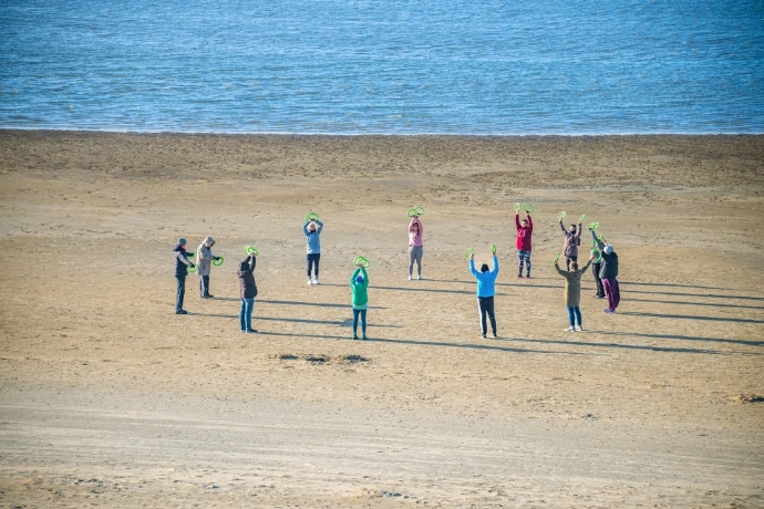 People exercising in a circle on a sandy beach.
